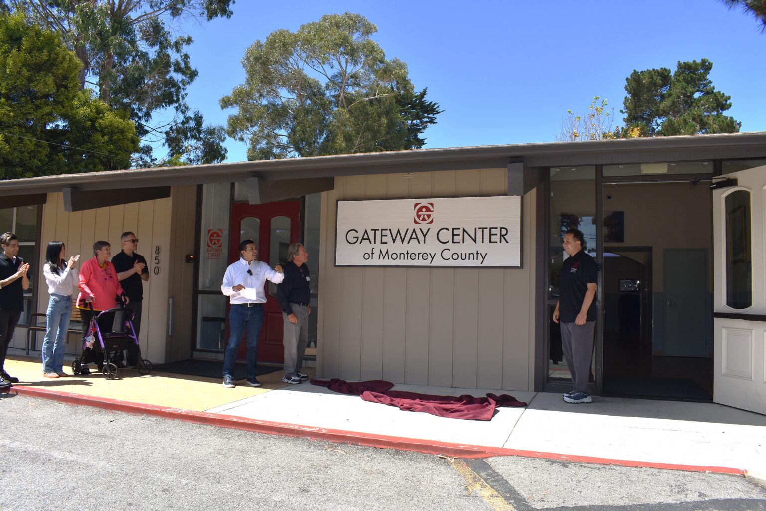 Gateway Center Executive Director & President Mike Gonzalez, Board Chair George Molano, and Community Day Program participant Hassan join staff and community members to unveil the new campus sign.